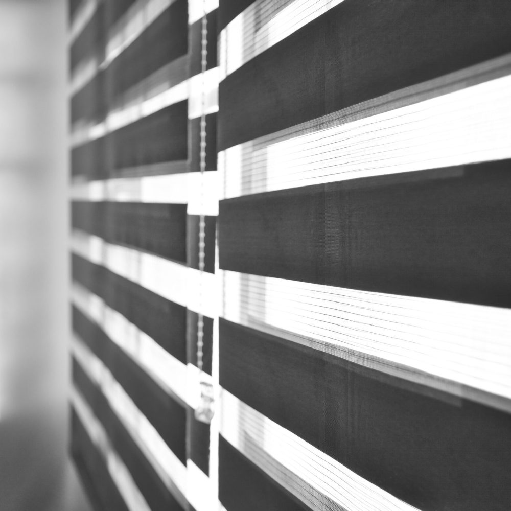 Sun shining through window roller blinds throwing shadows on the wall. Atmospheric mood. Selective focus.